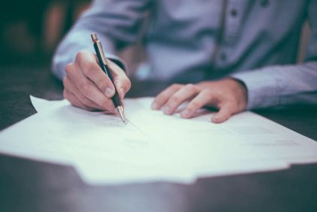 Homem assinando diploma em uma mesa, simbolizando o processo formal de como comprar um diploma legítimo e reconhecido pelo mec.